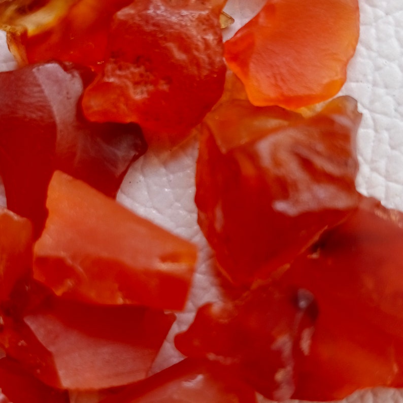 Puede incluir: Primer plano de una colecci&oacute;n de peque&ntilde;as piedras de cornalina de forma irregular. Las piedras son de color rojo anaranjado intenso y tienen una calidad transl&uacute;cida.