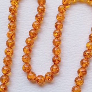 May include: A strand of amber beads, each bead is round and has a translucent orange colour with flecks of gold throughout.