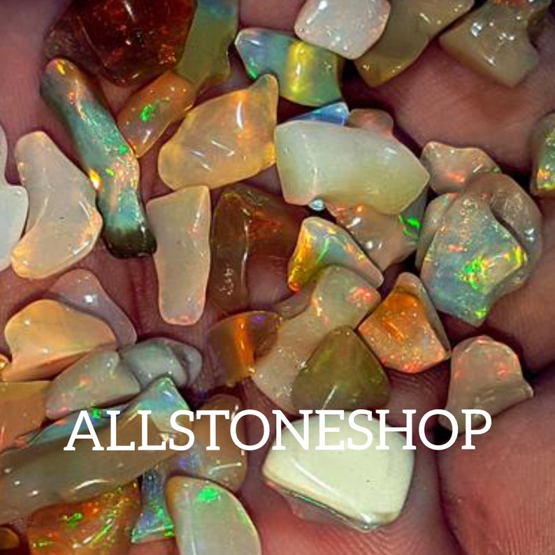 May include: A collection of iridescent opal chips in various shapes and sizes. The chips are a mix of white, brown, and green hues with flashes of color. The chips are displayed in a hand, with the text "ALLSTONESHOP" visible in the foreground.