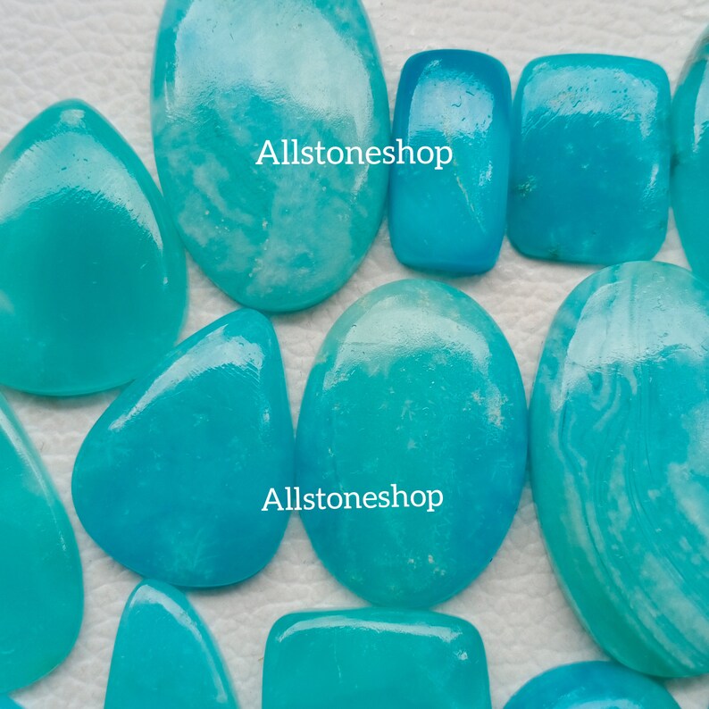 Puede incluir: Una colecci&oacute;n de diez piedras preciosas cabuj&oacute;n de color azul turquesa con vetas blancas. Las piedras son de diversas formas y tama&ntilde;os. El texto "Allstoneshop" aparece dos veces en la imagen.