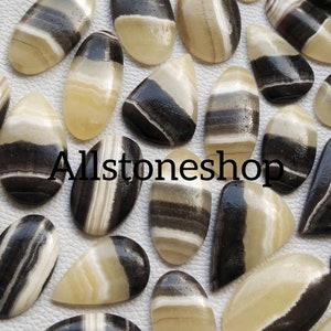 May include: A collection of 18 black and white banded agate cabochons, each with a unique pattern. The cabochons are oval shaped and have a smooth, polished finish. Allstoneshop is printed on the image.