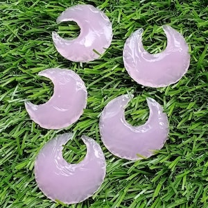 May include: Five pink crescent moon shaped arrowheads on a green grass background.