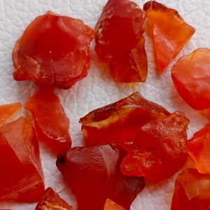 Puede incluir: Una colecci&oacute;n de piedras preciosas de cornalina roja, cada una con una forma y textura &uacute;nicas. Las piedras est&aacute;n dispuestas sobre una superficie blanca.