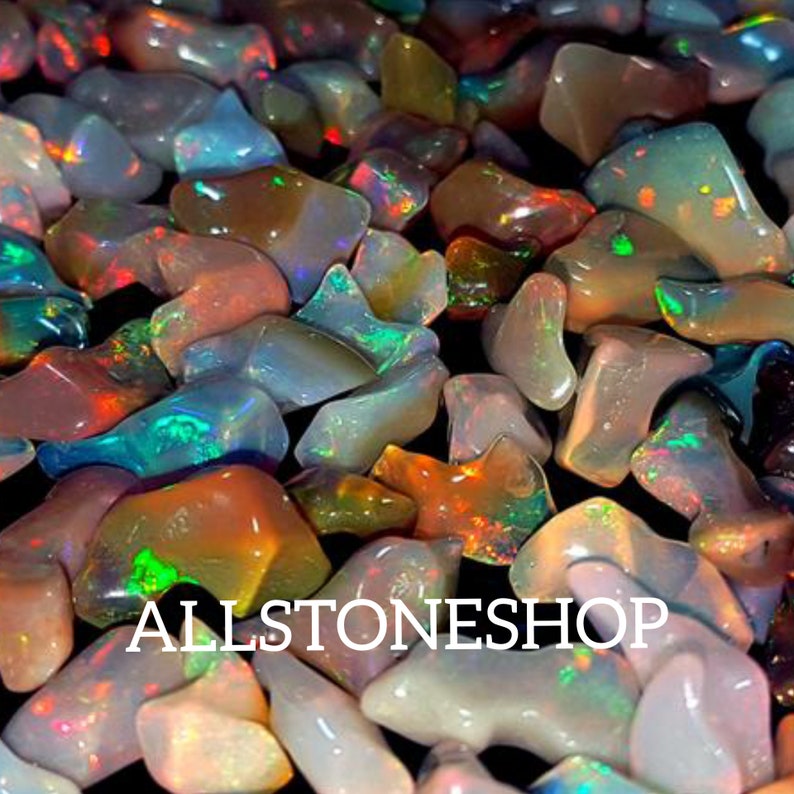 May include: A collection of iridescent opal gemstones in various shapes and sizes. The opals are a mix of white, pink, and blue with flashes of green and red.