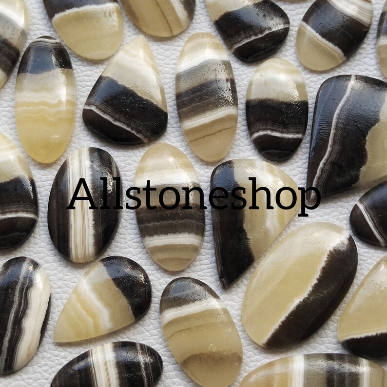 May include: A collection of 20 black and white banded agate cabochons. The cabochons are oval and teardrop shaped. The banding is natural and varies in width and color.