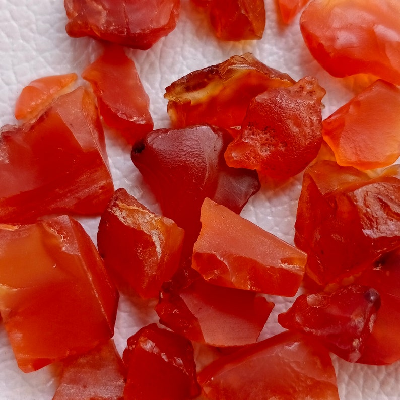 Puede incluir: Una colecci&oacute;n de piedras preciosas de cornalina de diferentes formas y tama&ntilde;os. La cornalina es de color rojo anaranjado intenso y tiene una superficie lisa y pulida.