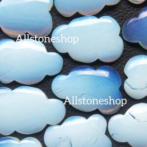May include: A collection of iridescent blue and white cloud-shaped cabochons. The cabochons are smooth and have a slightly translucent appearance. The text "Allstoneshop" is visible in the image.
