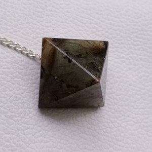 May include: A black and green crystal pyramid pendant on a silver chain. The pyramid is faceted and has a smooth, polished finish.