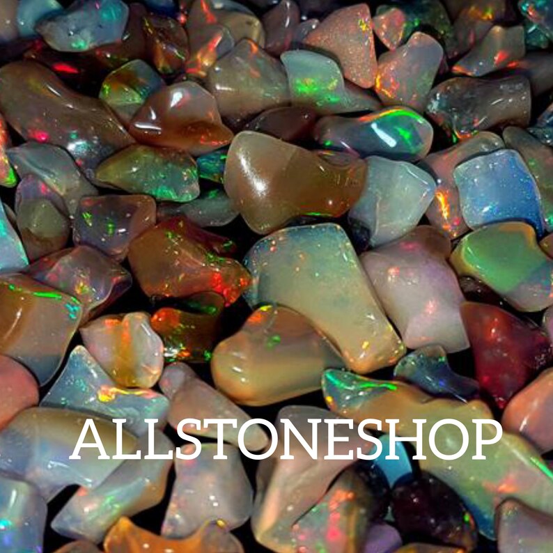 May include: A close-up of a collection of iridescent opal gemstones in various shapes and sizes. The opals are a mix of brown, green, and white with flashes of color. The text "ALLSTONESHOP" is visible in the center of the image.