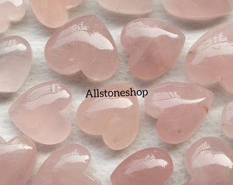 Puede incluir: Una colección de piedras de cuarzo rosa en forma de corazón. Las piedras son lisas y pulidas, con un aspecto natural y translúcido. Las piedras están dispuestas sobre una superficie blanca. Allstoneshop está escrito en la imagen.