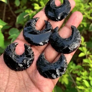 May include: Five black obsidian crescent moon shaped stones. The stones are smooth and polished with a glossy finish.