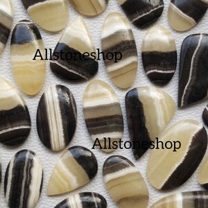 May include: A collection of 15 oval-shaped cabochon gemstones with black and white banded patterns. The stones are polished and have a smooth, glossy finish.