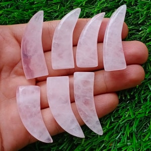 May include: Seven pink rose quartz crystal points shaped like fangs. The points are smooth and polished.