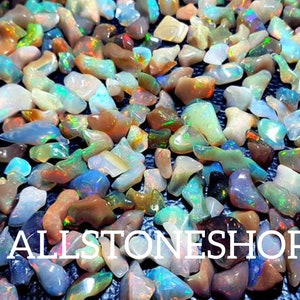May include: A large collection of iridescent opal chips in various shapes and sizes. The chips are a mix of white, brown, blue, green, and orange. The chips are scattered on a black surface. ALLSTONESHOP is written in white letters on the bottom of the image.