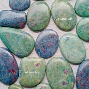 May include: A collection of polished gemstones in various shapes, including ovals and rectangles. The stones feature a mix of colors, including blue, green, and pink, with a marbled appearance. The text "Allstoneshop" is visible on some stones.