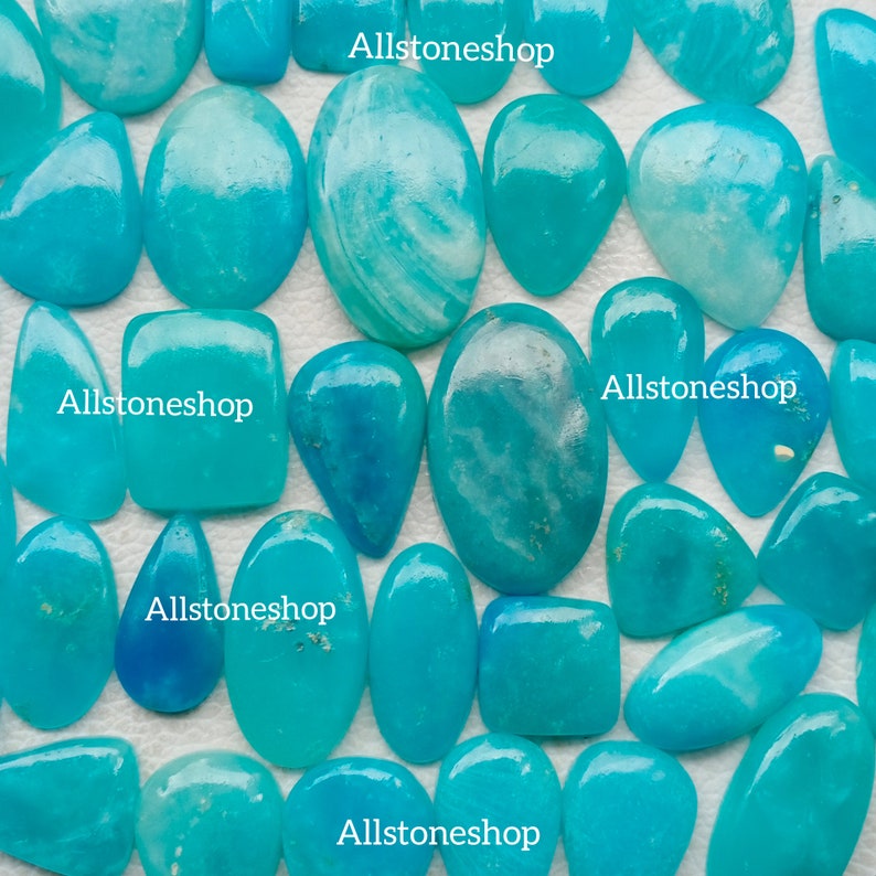 Puede incluir: Una colecci&oacute;n de 17 piedras preciosas cabuj&oacute;n de color azul turquesa de diversas formas y tama&ntilde;os. Las piedras son lisas y pulidas, con un ligero brillo. Allstoneshop est&aacute; impreso en la imagen.