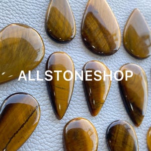 May include: A collection of ten teardrop-shaped tiger's eye stones. The stones are a mix of light and dark brown with a golden sheen.