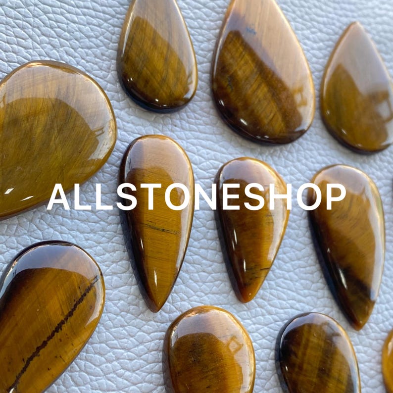 May include: A collection of ten teardrop-shaped tiger's eye stones. The stones are a mix of light and dark brown with a golden sheen.
