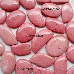May include: A collection of pink and white polished stones, some with a smooth oval shape and others with a more irregular shape. The stones are arranged on a white surface. The text "Allstoneshop" appears three times in the image.