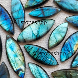 May include: A collection of 12 iridescent blue and green labradorite gemstone cabochons in a marquise shape. The stones have a pearlescent sheen and are perfect for jewelry making.