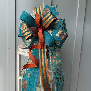 May include: Teal, orange, and gold ribbon bow with a leopard print ribbon. The bow is tied around a white lantern.