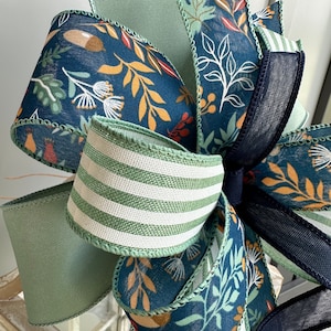 May include: A decorative bow made with three different ribbons. The ribbons are a blue and white floral print, a green and white striped ribbon, and a solid green ribbon. The bow is tied with a black ribbon.