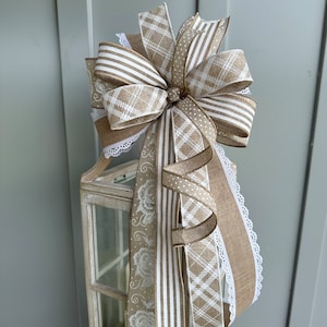 May include: A brown and white plaid ribbon bow with a white lace trim, tied around a white lantern.