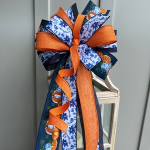 May include: A blue and orange ribbon bow with a pumpkin pattern. The bow is tied around a lantern.