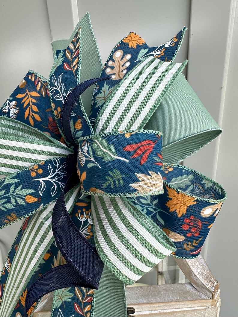 May include: A fall-themed bow featuring a blue and green floral print, green and white striped ribbon, and a solid navy blue ribbon.