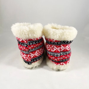 Puede incluir: Un par de zapatillas de estar por casa con estampado rojo, blanco y negro con forro de piel sint&eacute;tica blanca.