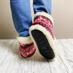 Puede incluir: Pantuflas de punto con estampado rojo y negro, forro de piel sint&eacute;tica blanca y suelas de goma negra.