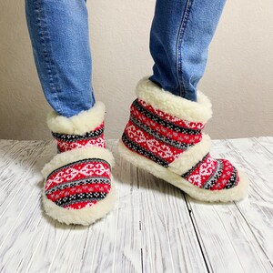 Puede incluir: Pantuflas de forro polar con estampado rojo y blanco y un pu&ntilde;o blanco peludo. Las pantuflas se llevan en los pies de una persona.