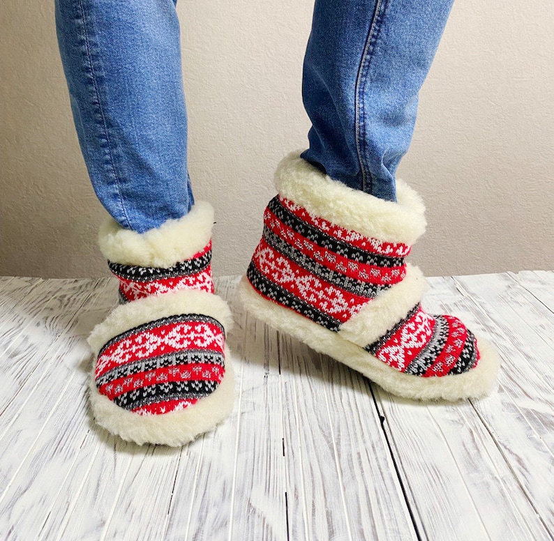 Puede incluir: Pantuflas de forro polar con estampado rojo y blanco y un pu&ntilde;o blanco peludo. Las pantuflas se llevan en los pies de una persona.