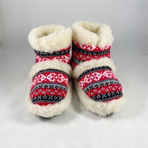 Puede incluir: Un par de zapatillas rojas, blancas y negras con un forro blanco y esponjoso. Las zapatillas tienen un dise&ntilde;o de punto.