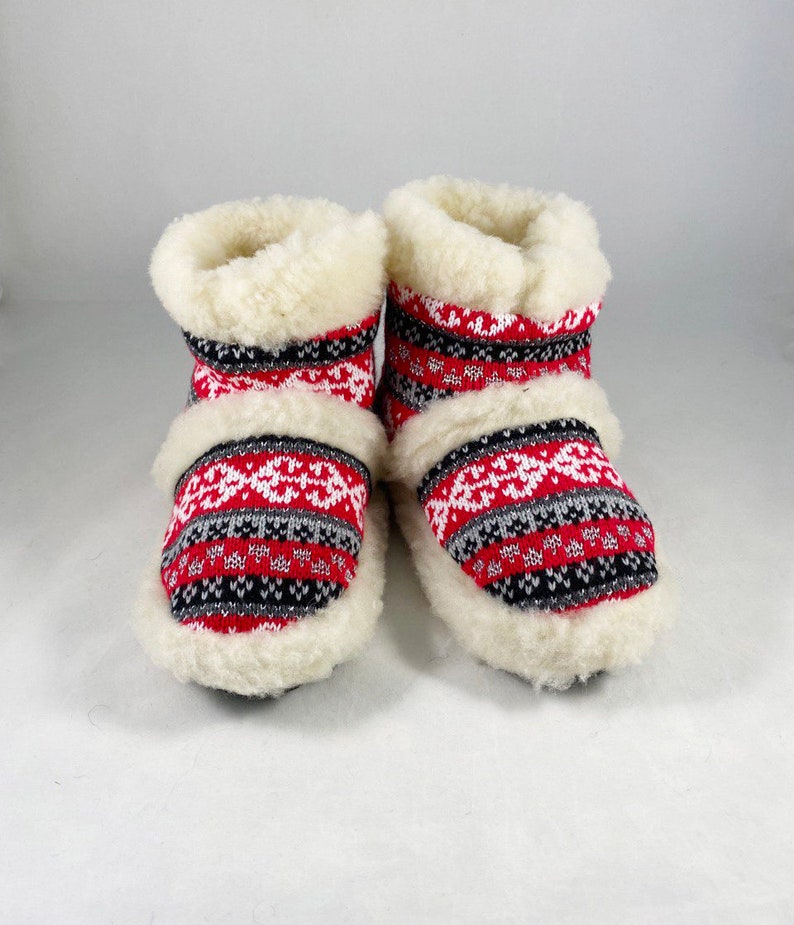 Puede incluir: Un par de zapatillas rojas, blancas y negras con un forro blanco y esponjoso. Las zapatillas tienen un dise&ntilde;o de punto.