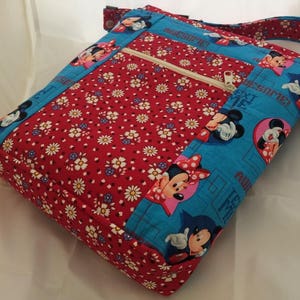 Puede incluir: Un bolso bandolera de tela rojo y azul con un bolsillo con cremallera y un estampado de Mickey Mouse y Minnie Mouse. El bolso tiene un estampado de margaritas blancas en la solapa delantera y las palabras "Awesome!" impresas en el lateral.