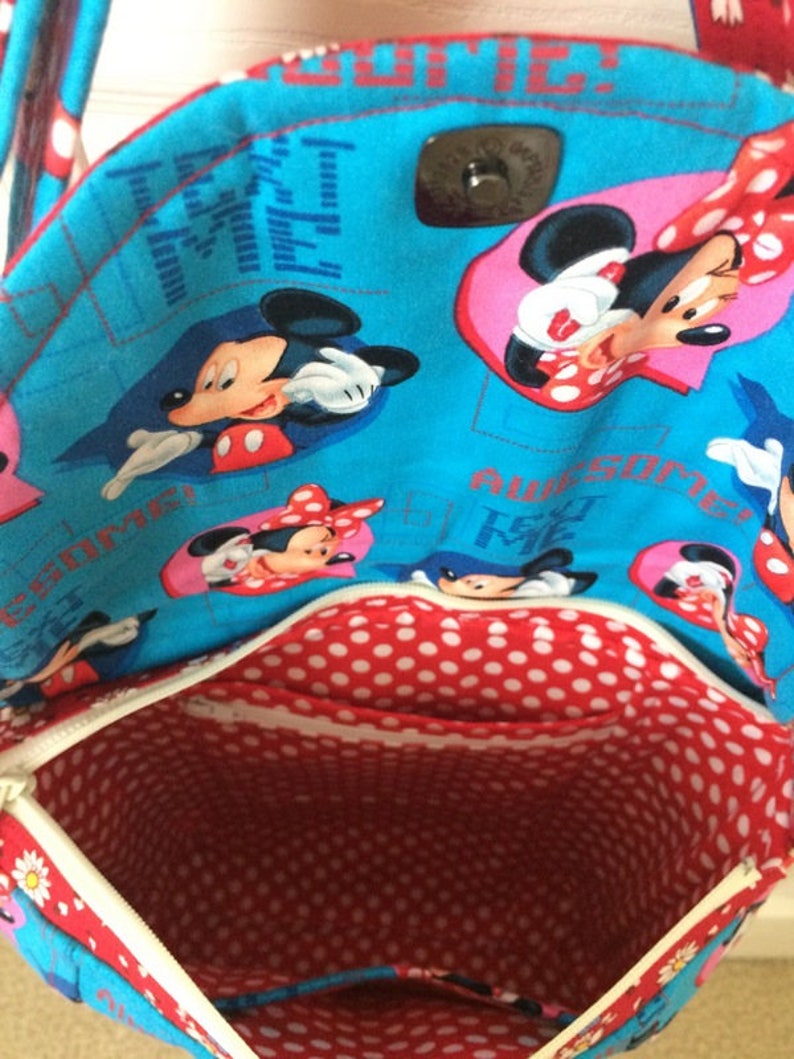Puede incluir: Una bolsa de tela azul y roja con cierre de cremallera. La bolsa est&aacute; decorada con un patr&oacute;n repetido de personajes de Mickey Mouse y Minnie Mouse. El texto "Text Me" y "Awesome" est&aacute; impreso en la bolsa.