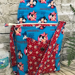 Puede incluir: Un bolso bandolera de tela azul y roja con cierre de solapa. El bolso presenta un estampado floral y un estampado repetido de personajes de Mickey Mouse y Minnie Mouse con el texto "Text Me" y "Awesome!" impreso en la tela.