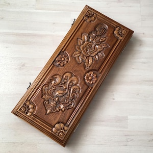May include: A wooden box with intricate carvings of flowers and leaves. The box is a rich brown color and has a polished finish.