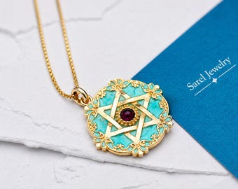 May include: A gold-tone necklace featuring a circular pendant with a turquoise inlay and a central dark red stone. The pendant displays a six-pointed star design surrounded by ornate filigree metalwork. The text Sarel Jewelry is visible.