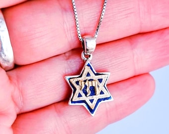 May include: A silver necklace featuring a Star of David pendant. The pendant has a blue enamel background with gold-colored trim and Hebrew lettering. The necklace is displayed against a light background.