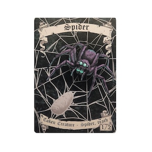Puede incluir: Una carta de fantasía que presenta una araña morada con ojos verdes sobre una telaraña, con la palabra "Spider" en una pancarta. Debajo de la araña hay un capullo y el texto "Token Creature - Spider, reach 1/2".