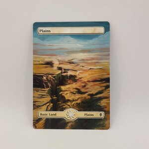 May include: A Magic: The Gathering card depicting a landscape with a canyon and a waterfall. The card is titled "Plains" and is a basic land card.
