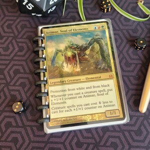 Puede incluir: Una carta de Magic: The Gathering con borde dorado con una ilustración verde, marrón y blanca de una criatura llamada "Animar, Alma de los Elementos". El texto de la carta dice "Criatura legendaria - Elemental". La carta tiene una fuerza y resistencia de 1/1.