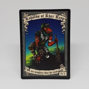 May include: A trading card featuring a red and green goblin-like creature with a spiked club. The card is titled "Kobolds of Kher Keep" and has the text "We are mightier than the cockroach!"  0/1