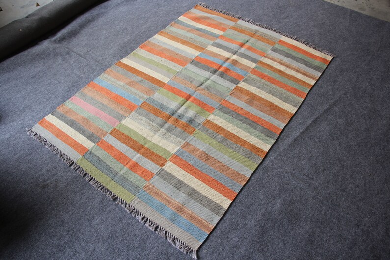May include: A rectangular rug with a striped pattern in shades of orange, blue, green, and gray. The rug has a fringe border.