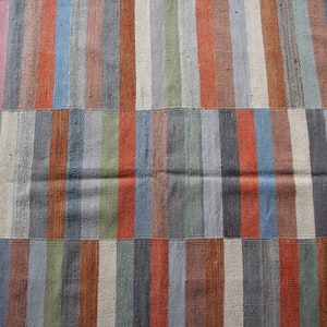 May include: A close-up of a woven rug with a striped pattern in shades of blue, green, brown, and orange.