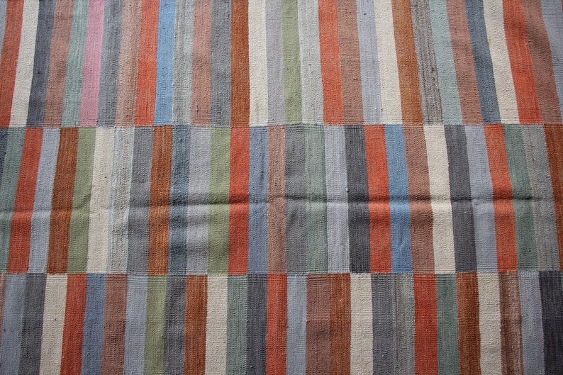 May include: A close-up of a woven rug with a striped pattern in shades of blue, green, brown, and orange.
