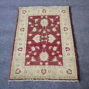 May include: A red rug with a cream-colored border and floral pattern. The rug has a fringe border.