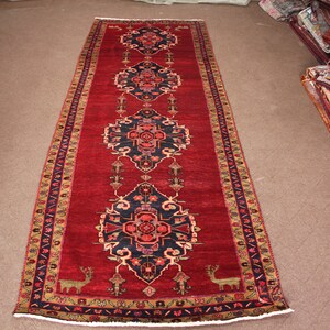 K&ouml;nnte beinhalten: Ein langer roter L&auml;uferteppich mit traditionellem persischem Design. Der Teppich hat eine dunkelblaue Mitte mit komplizierten Blumenmustern und einen gold-schwarzen Rand.